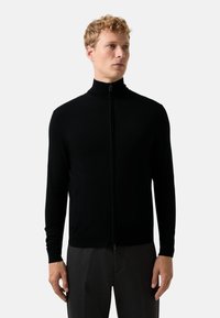 Černý svetr na zip s vysokým límcem a dlouhými rukávy. Vyrobený z hladkého materiálu, s bočními kapsami a přiléhavým střihem.