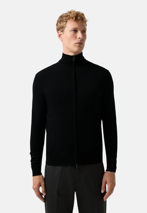 Black zip-up sweater with a high collar and long sleeves. Made of a smooth fabric, featuring side pockets and a fitted silhouette.