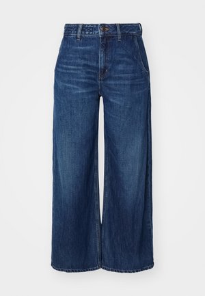 Jeans a gamba larga in denim blu scuro. Presentano una vita alta, una chiusura con bottone e tasche frontali. Il tessuto ha una trama morbida con cuciture visibili.
