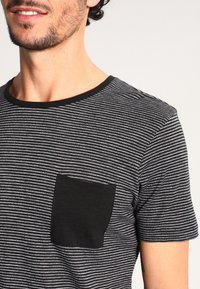 Svart-och-vit randig t-shirt med kort ärm, solid svart bröstficka och rund halsringning, tillverkad av ett lätt material.