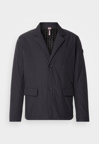 Chaqueta negra texturizada con collar de solapa, dos bolsillos frontales y dos botones. Diseño ligero con un forro interior suave.