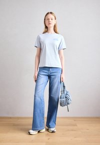 Lyseblå t-skjorte med korte ermer med teksten "LOVE CRUSH", kombinert med lyseblå flared jeans og en liten, teksturert blå håndveske.