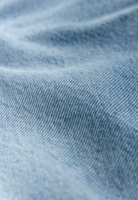 Textură de denim albastru deschis, cu aspect neted, ușor estompat, prezentând o țesătură în diagonală vizibilă și variații subtile de culoare.