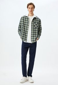 Grön och marinblå rutigt flanellskjorta med vit krage, kombinerad med mörk denimbyxor och vita sneakers. Har en bröstficka.