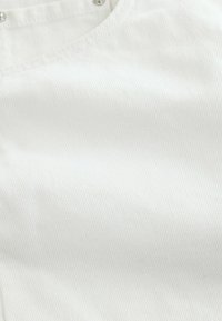 Haut blanc sans manches en maille côtelée avec un col en V et trois petits boutons à l'avant près de l'encolure.