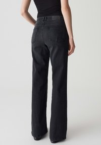 Jeans en denim noir avec un design à jambe droite, présentant une taille haute, deux poches arrière et une étiquette texturée à la taille.