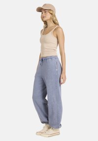 Beżowy podkoszulek o prążkowanej strukturze, zestawiony z luźnymi, jasnobłękitnymi spodniami dresowymi z kieszeniami i sznurkiem do regulacji.