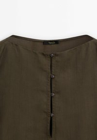 Blouse vert olive avec un col rond, présentant une patte de boutonnage verticale avec cinq boutons foncés et une texture subtile.