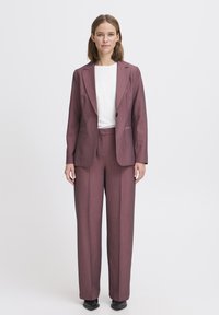 Completo color bordeaux con blazer sartoriale e rever a punta, pantaloni a vita alta. Top bianco sotto, tessuto morbido e scarpe basse.