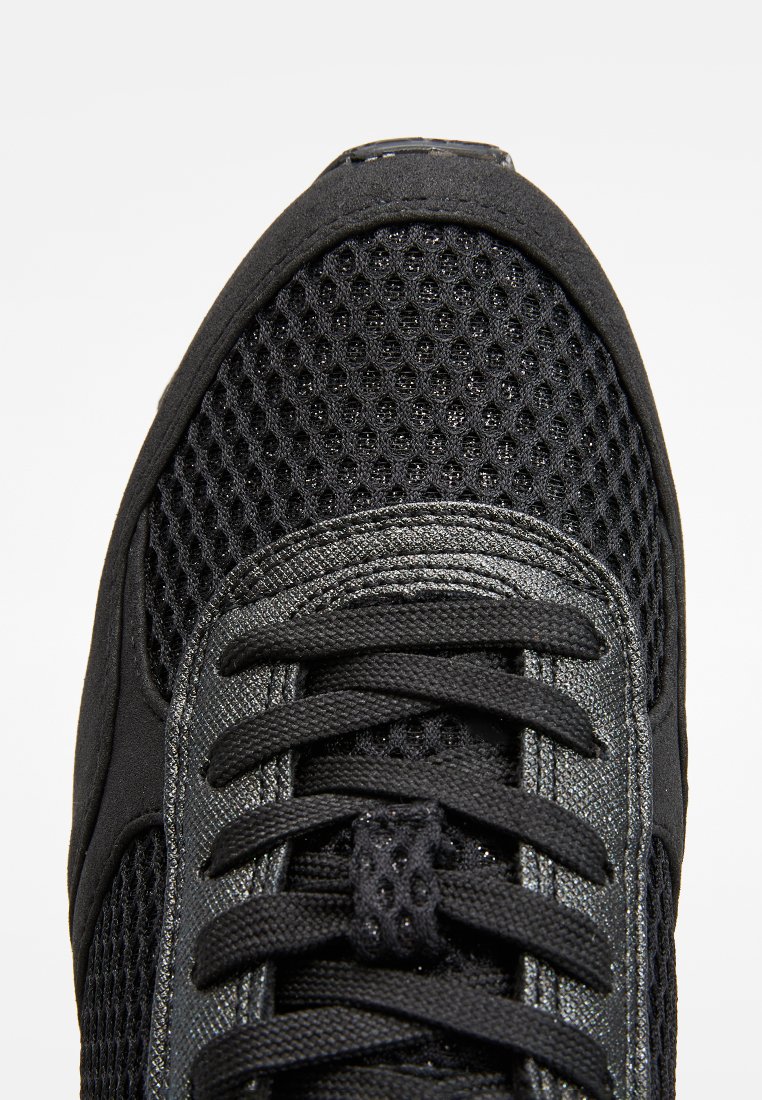 Basket noir avec une tige en mesh, des superpositions synthétiques texturées, des lacets plats et une languette rembourrée, offrant un design épuré et une semelle en caoutchouc.