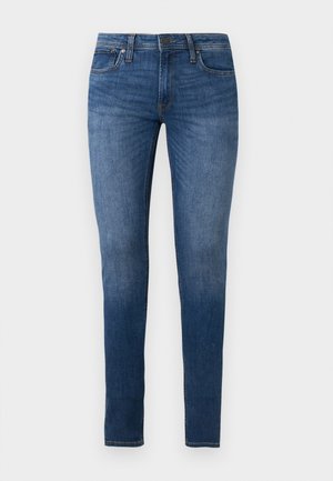 Jean skinny bleu avec un lavage moyen, design cinq poches, fermeture par bouton et passants pour ceinture, présenté sur fond blanc.
