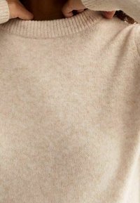 Helles beiges Sweater aus weichem Strickmaterial mit einem gerippten runden Ausschnitt und Bündchen, der eine subtile Textur und ein zurückhaltendes Design aufweist.