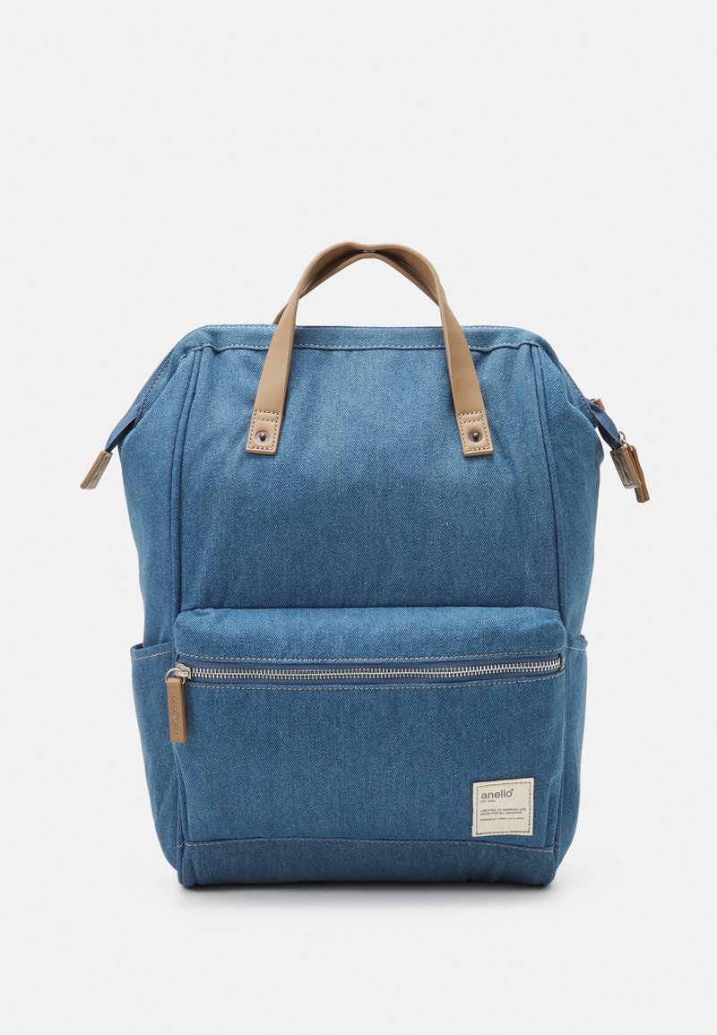 Denim backpack in blue with tan leather handles, front zipper pocket, and stitched detailing. Features a structured, upright design.