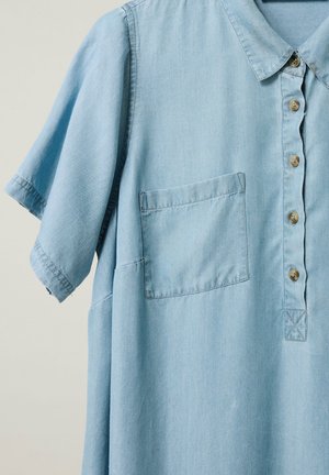 Vaaleansininen lyhythihainen paita, jossa on kaulus, vasemmalla puolella etutasku ja viisi ruskeaa nappia edessä.