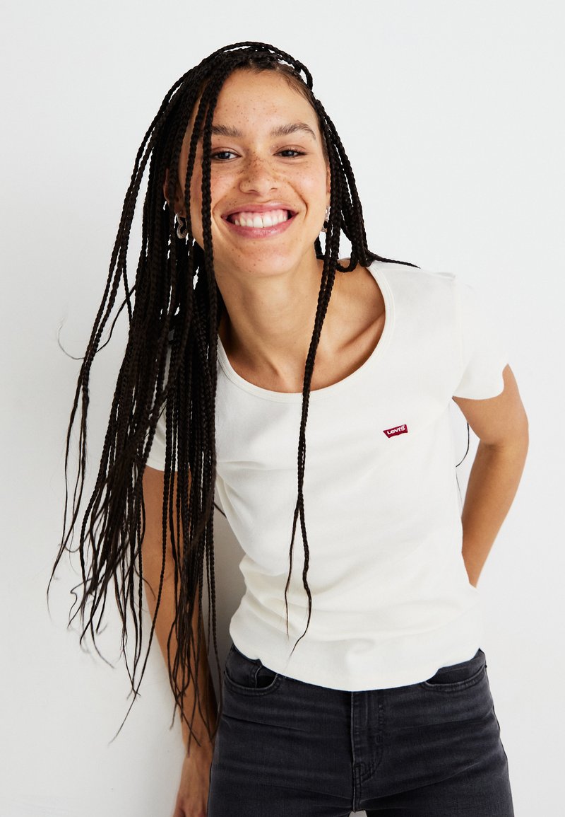 T-shirt en coton blanc avec un col rond et des manches courtes, ornée d'un petit logo rouge Levi's sur la poitrine gauche, associée à un jean foncé.
