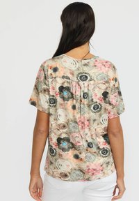 Kortermet skjorte i lett stoff med blomstermønster i rosa, svart og blå akenter. Rund hals og detaljer med legg på ryggen.