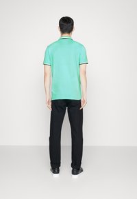 Grön polo skjorta med svart och vit randig krage, i kombination med svarta byxor. Outfiten har en avslappnad passform och en enkel design.