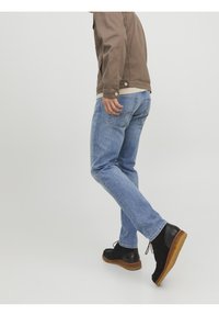 Vaqueros de mezclilla azul claro con corte recto, combinados con botines negros de ante con suela color canela. Fondo gris neutro.