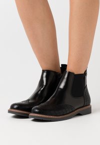 Black leather ankle boots with elastic side panels, textured crocodile pattern on the toe, and brown stitching around the sole.