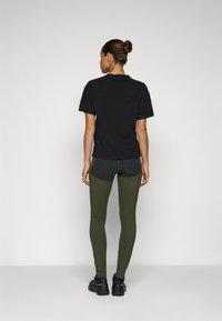 Svart kortärmad träningströja med en avslappnad passform, tillsammans med olivgröna leggings med en snygg design och grå detaljer. Svarta skor.
