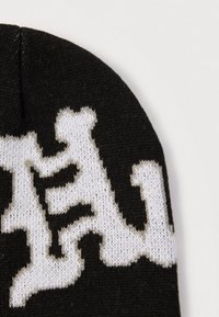 Căciulă neagră tricotată, cu un model abstract alb contrastant, material texturat, formă rotunjită și margine subtil zimțată.