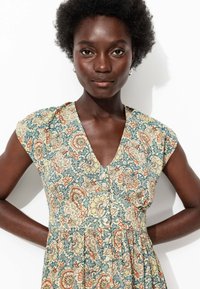 Robe à imprimé floral avec un décolleté en V, des manches courtes et une taille froncée. Les couleurs incluent beige, bleu et orange dans un tissu texturé.
