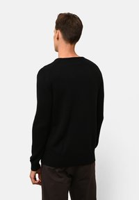 Zwarte gebreide trui met lange mouwen, ronde halslijn en geribde zoom. Het materiaal lijkt zacht en textured, weergegeven vanuit de achterkant.