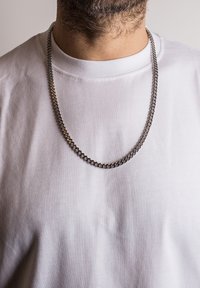 Collana in metallo con maglie in argento e oro, poggiata su una semplice t-shirt bianca. Le maglie sono spesse e intrecciate.