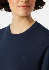 Marinblå sweatshirt med rund hals, med en subtil broderad logotyp i en något mörkare nyans av blått. Slät, bomullsliknande textur.