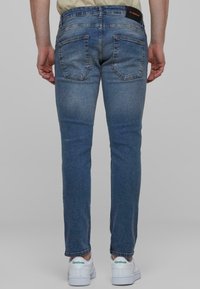 Slim fit traperice u srednjem pranju, s pet džepova, klasičnim pojasom i suptilnim izbljeđenjem. Uparene s bijelim tenisicama.