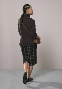 Pulover închis la culoare, cu guler înalt și manșete răsucite, asortat cu o fustă până la genunchi, cu carouri în alb și negru. Pantofi negri și o geantă de umăr maro.