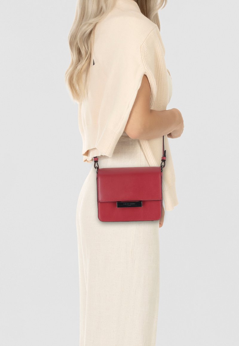 Red leather crossbody bag with a flat design, magnetic flap closure, and a black hardware accent. Smooth texture, sleek shape, adjustable strap.