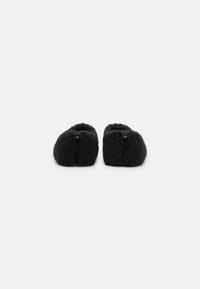 Black slip-on slippers with a textured, fluffy exterior, rounded shape, and minimalistic design, featuring a subtle logo accent on the back.