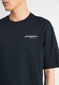 Black cotton t-shirt with a round neck, featuring white "JORDAN Racing" text on the left chest. Short sleeves, no patterns.
