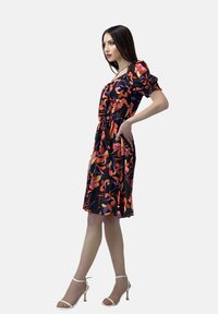 Vestido negro con patrones florales coloridos en naranja y púrpura. Cuerpo fruncido, mangas cortas abullonadas y dobladillo a la altura de la rodilla.