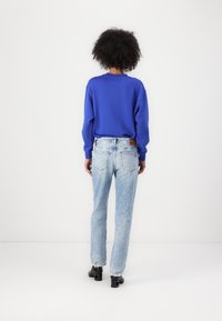 Sudadera azul de manga larga, combinada con jeans rectos en un tono azul claro y desgastados. Botas negras de tacón completan el conjunto.