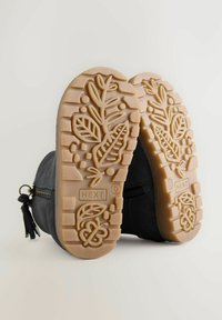 Botine negre din suede, până la gleznă, cu un fermoar lateral, având o talpă din cauciuc texturată, bej, cu modele de frunze și un accent de ciucure.
