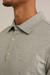 Světle šedé pruhované polo tričko s límečkem na knoflíky, má jedno kapsičku na hrudi a světlé knoflíky. Hladká textilie.