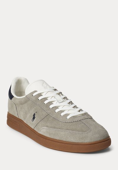 Világosszürke velúr sportcipő fehér fűzőkkel, barna gumi talppal, sötétkék sarokpárnával és kis sötét logóval az oldalán.