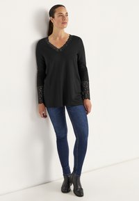 Svart långärmad topp med en spets V-ringning och spetsdetaljer på ärmarna. Matchad med figurnära mörkblå jeans och svarta ankelboots.