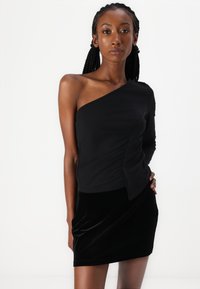 Zwarte one-shoulder top met gedrapeerd ontwerp en lange mouw, gecombineerd met een zwarte fluwelen minirok, met een gladde textuur en een getailleerde silhoeet.