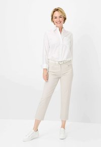 Weißes, langärmliges Hemd mit Knopfverschluss, kombiniert mit hellbeigen, strukturierten, cropped Hosen und weißen Sneakers. Das Outfit zeigt einen lässigen Stil.