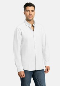 Camisa blanca de manga larga con botones, cuello tipo polo, tejido texturizado y dobladillo recto. Llevada con jeans azules.