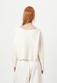 Cream-colored cropped sweater with a loose design, wide neckline, and long sleeves. Soft texture with raw hem detailing at the bottom.