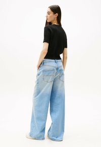 Top corto a maniche corte di maglia nera con texture a coste abbinato a jeans in denim blu chiaro a gamba larga con due tasche posteriori.