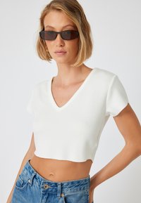 Hvid cropped V-hals t-shirt lavet af blødt stof med korte ærmer, parret med højtaljede blå denim jeans.