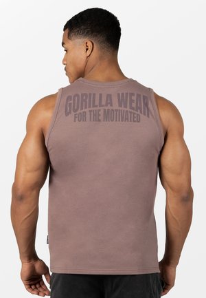 Gespiereerde man met zijn rug naar ons toe, die een bruine mouwloze shirt draagt met de tekst "GORILLA WEAR FOR THE MOTIVATED" op de rug.