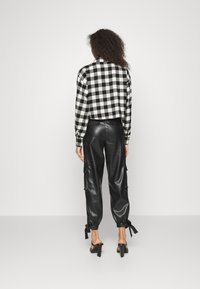 Schwarz-weißer karierten Crop-Top kombiniert mit hochgeschnittenen schwarzen Kunstlederhosen, die seitliche Taschen und Knöchelbindungen haben. Schwarze Absätze.