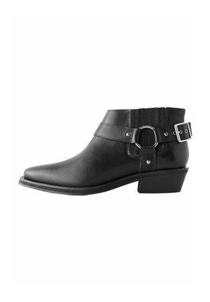 Bottine noire en cuir avec bout pointu, petit talon bloc, bride décorative, boucle argentée et détail anneau sur le côté.