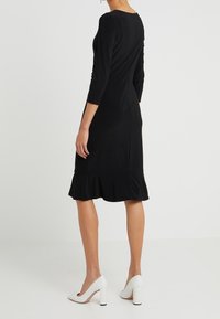 Czarna sukienka do kolan z rękawami 3/4, dopasowanym krojem i falbaniastym wykończeniem. Uzupełniona białymi szpilkami.